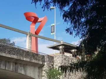 La Antorcha de la Amistad rising above a stone wall beside the riverwalk under a blue sky.