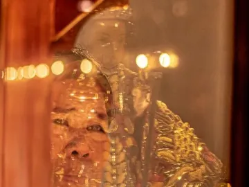 Santo Niño de Cebú in gold-toned robes with a person’s face and outstretched hand reflected over the image.