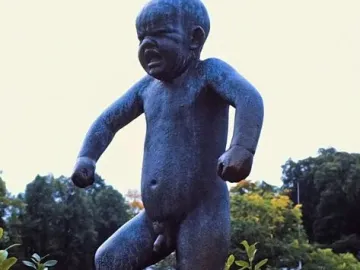 The Sinataggen bronze sculpture of a toddler stamping its foot on a pedestal, surrounded by trees.