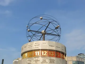 The World Time Clock in Berlin, with city names and illuminated time panels beneath a spherical metal top in a public plaza.