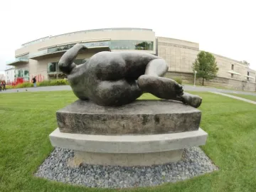 The River by Aristide Maillol, a dark recumbent nude sculpture on a pedestal in a sculpture garden.