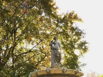 Diana Fountain in a grassy garden with autumn leaves and tall trees behind it.