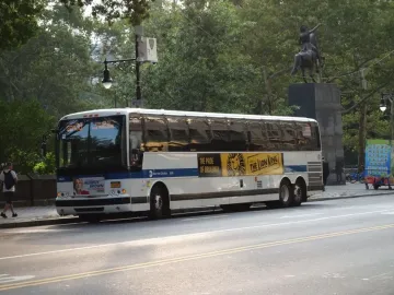 Simón Bolívar Equestrian Statue seen above a white bus, with the rider on horseback silhouetted against trees.