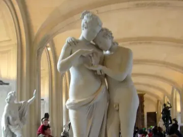 Standing Psyche and Love marble sculpture displayed on a pedestal in a museum gallery with visitors in the background.