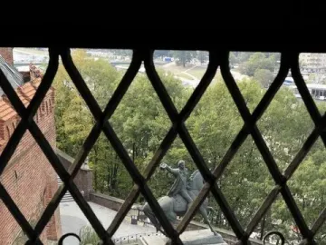 Tadeusz Kościuszko Monument seen through a dark window grate, showing a bronze equestrian statue on a pedestal.