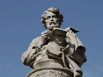 Gavarni Fountain stone sculpture with a carved figure holding an open book and pen against a blue sky
