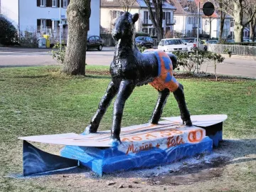 Holbeinpferd sculpture painted with an orange and blue pattern on its hindquarters, standing on a surfboard-like base.