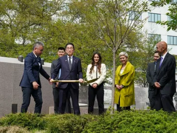 People in formal attire stand near the Japanese American Memorial with a gold shovel during a ceremonial gathering.