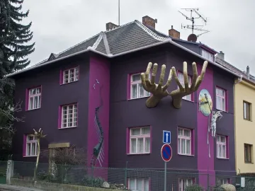 Kristek House with a dark purple facade, magenta accents, golden hands, a melting figure on a clock, and a mural of a winding train track.