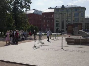 The Solovetsky Stone stands on a dark base in a paved square, with people gathered nearby behind metal barriers.