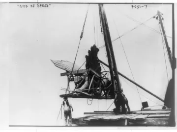 Golden Boy statue being hoisted by cables and a wooden framework with workers below.