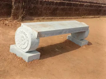 A long granite bench with a carved floral support at Gomateshwara.