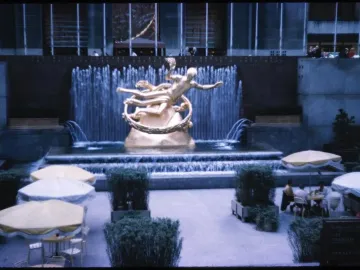 The Prometheus sculpture at Rockefeller Center, shown as a golden reclining figure holding up a ring above a tiered fountain.