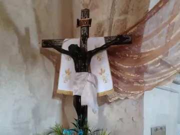 San Juan Patrón crucifix with a dark-skinned corpus, white loincloth, and red, white, and blue flowers below