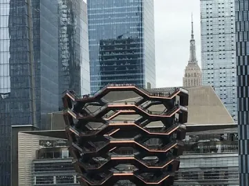 The Vessel sculpture in Manhattan, with honeycomb-like stairways beside glass skyscrapers and train tracks in the foreground.