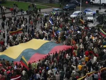 Large crowd holding a huge yellow green and red flag near the Bronze Soldier monument.