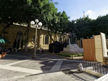 Great Siege Monument with three bronze figures in a sunny paved plaza surrounded by trees and historic buildings.