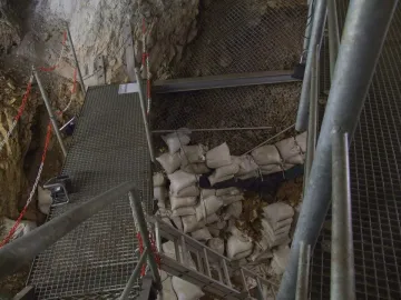 Archaeological excavation site inside the Hohle Fels cave with metal walkways, stairs, and sandbags among rocky walls.