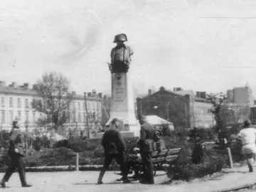 Monument to Napoleon Bonaparte on a tall plinth in a park, with people sitting and walking nearby.