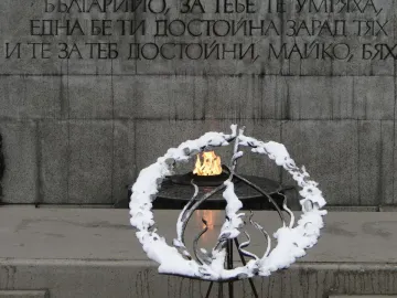 The Unknown Soldier Monument with a grey stone wall, Cyrillic inscription, and an eternal flame in a dark metal basin.