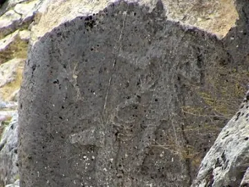 Karasu relief carved on a weathered dark stone slab among larger rocks.