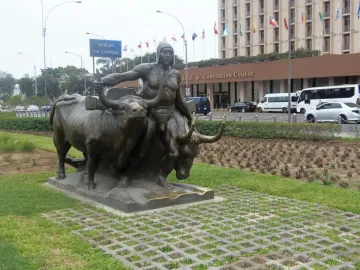 La yunta bronze sculpture of a man guiding two oxen on a lawn beside a patterned walkway.
