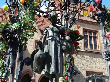 Gänseliesel Fountain with a bronze girl statue holding geese, decorated with Easter eggs and greenery.