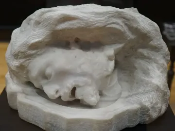 Head of Saint John the Baptist, a textured stone sculpture of a face with closed eyes and an open mouth set in a rough enclosure.