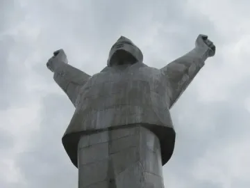 Monument to Stjepan Filipović seen from below, with the figure raising both arms against a cloudy sky.