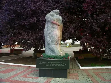 The Shot in the Back monument showing two stone figures on a dark base with Cyrillic text, set among trees and paved paths.