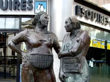 Monument to the Unknown Woman Worker, with two bronze women statues on a sidewalk beside a modern building.