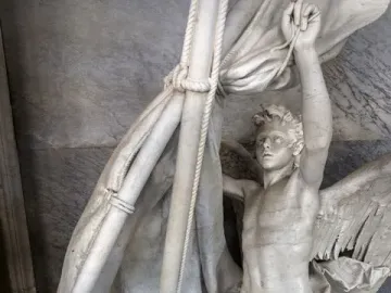 Angelo Nocchiero, a winged marble angel standing in a boat and holding ropes beside a mast and furled sails.