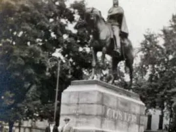George Armstrong Custer monument with a horse and rider atop a multi-tiered stone pedestal, with two people standing nearby.