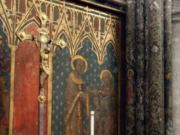 Gero Cross crucifix with a gilded Christ figure on a dark cross before a painted religious mural.