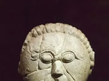 Mšecké Žehrovice Head showing a carved stone face with oval eyes, a curled mustache, and a braided headdress.
