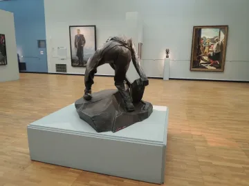 Cobblestone, a dark bronze headless figure crouching and holding a large stone.