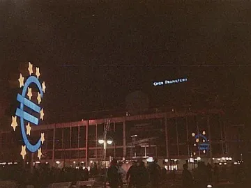 Illuminated Euro Sculpture with yellow stars in front of the Oper Frankfurt building at night.