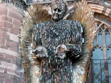 Knife Angel sculpture with outstretched hands and feathered wings outside a stone cathedral.