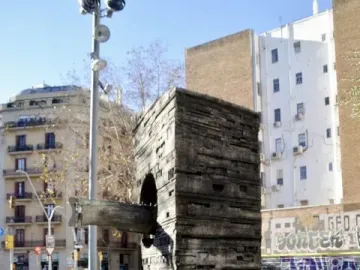 Monument to Narcís Monturiol, a tall textured concrete block with a submarine-like metal model protruding from its side, on a city sidewalk.