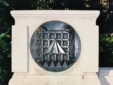 W.S.P.U. prisoners\' badge plaque on the Pankhurst Memorial stone plinth, with foliage in the background.