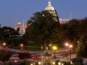 Bartholdi Fountain lit at dusk with water spraying into a circular basin, with the illuminated Capitol dome in the background.