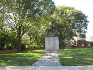 Bernardo de Gálvez equestrian statue on a tall stone pedestal surrounded by trees.