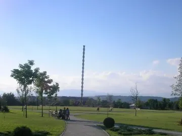 The Endless Column rises above a green park with trees, paths, and distant mountains.