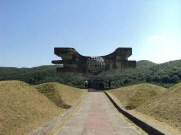 The Monument to the Revolution of the People of Moslavina, a large angular concrete sculpture with a circular center, standing among green hills.