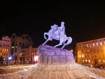 The Monument to Bohdan Khmelnytsky lit in purple, with a bright cluster of white lights at its base in a nighttime city square.