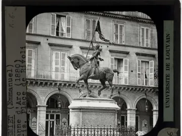 Joan of Arc equestrian statue on a tall pedestal in front of a building with arched shops and shuttered windows.