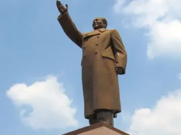 Bronze monument of Mao Zedong with his right arm raised, surrounded by smaller figures at the base.