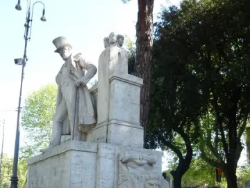 Monument to Giuseppe Gioachino Belli with a statue of a man in a top hat and long coat, beside a fountain with a grotesque face and round basin.