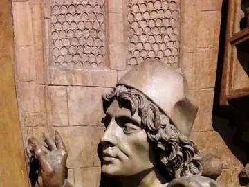 Wooden sculpture of Saint Luke in profile with raised hands and draped robes.
