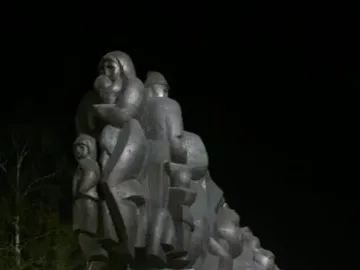 The Train of Pain monument showing a dark sculptural relief of families and children on a stone base at night.